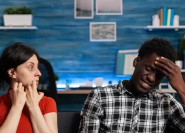 Interracial couple getting into argument sitting on couch. Irritated mixed race partners fighting and having relationship problems. Caucasian woman yelling at african american man