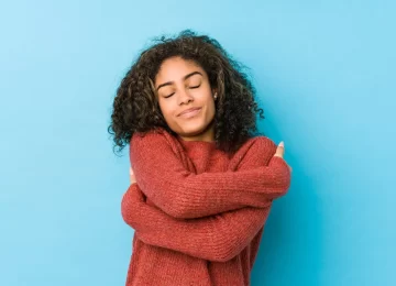 Young african american curly hair woman hugs, smiling carefree and happy.