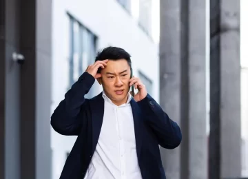 angry and serious Successful Asian businessman explains information to employees using phone, speaks near office outside