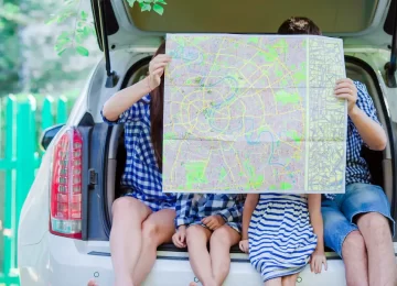 30478808_family-with-two-kids-looking-at-map-while-traveling-by-car-e1612646736539