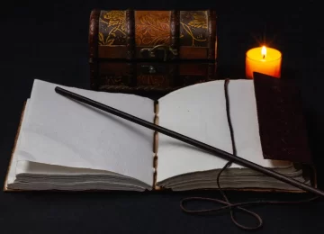 Image of open magic book and wand on the table in the dark room.