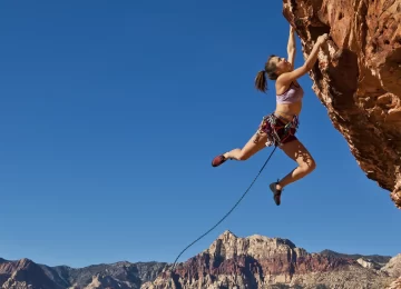 Female rock climber dangling on the edge of a steep cliff struggles for her next grip.