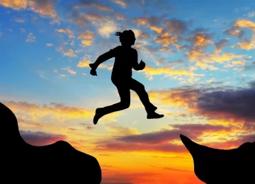 Woman jump over canyon at a sunset